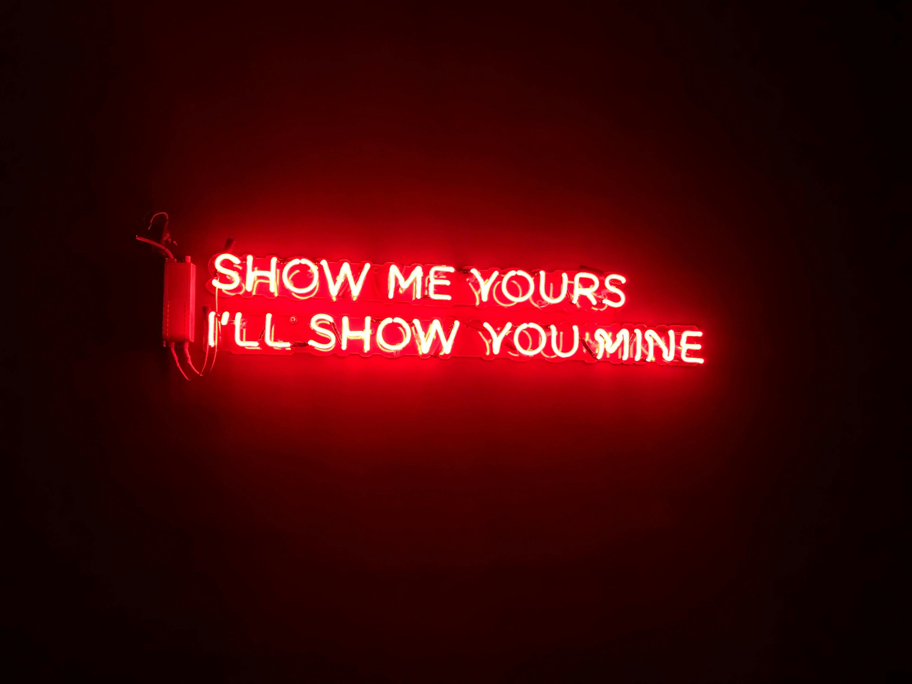 Neon sign reads show me yours, I'll show you mine